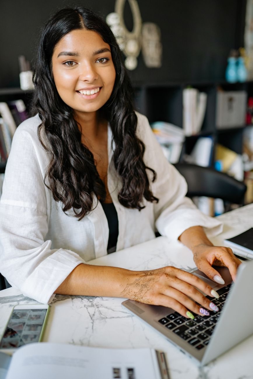 Confident young woman working on a laptop, smiling — representing the possibility Elevar opens up.